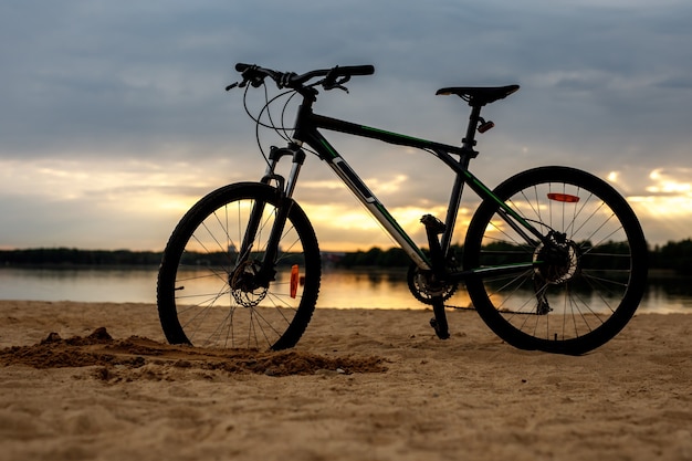 Siluetta della bicicletta sportiva su una spiaggia. Tramonto.