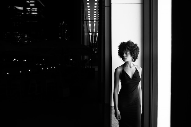 Siluetta della donna afroamericana in un vestito su una parete illuminata da una finestra. Elegante ritratto in bianco e nero