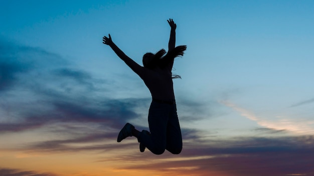 Siluetta della donna che salta nell'aria al tramonto