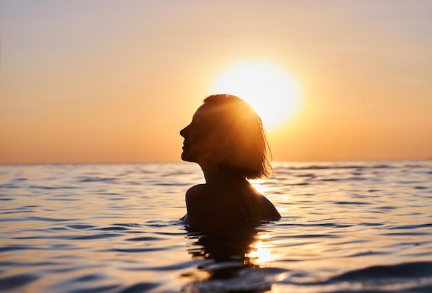 Siluetta della donna che si rilassa in acqua al tramonto nello stile della sensibilità emotiva serena facce retroilluminazione gioiosa e ottimista