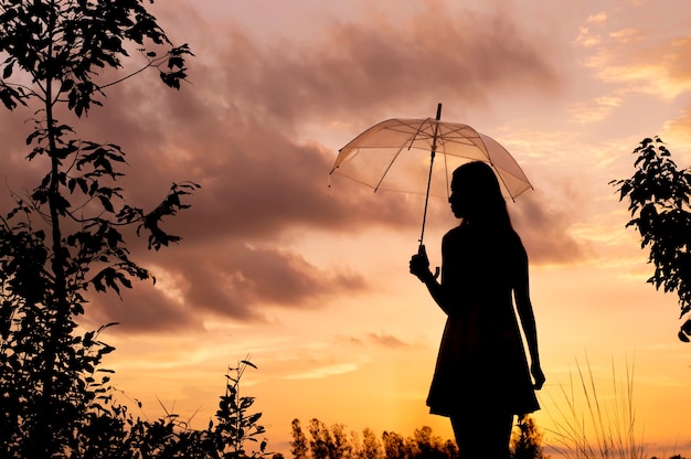 Siluetta della donna che tiene un ombrello con il cielo al tramonto