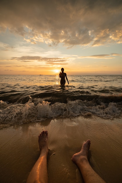 Siluetta della donna sulla spiaggia al tramonto con le gambe dell'uomo