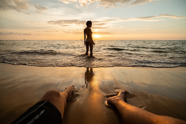 Siluetta della donna sulla spiaggia al tramonto con le gambe dell'uomo.