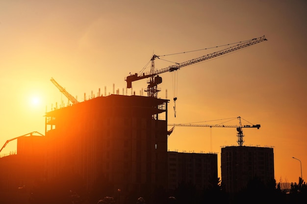 Siluetta della gru di costruzione che costruisce una casa su un cantiere sullo sfondo del cielo di tramonto