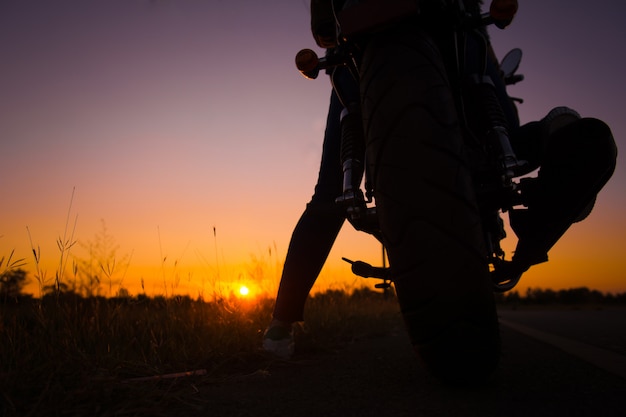 Siluetta della guida della giovane donna con la motocicletta sulla via, godente della libertà e della vita attiva