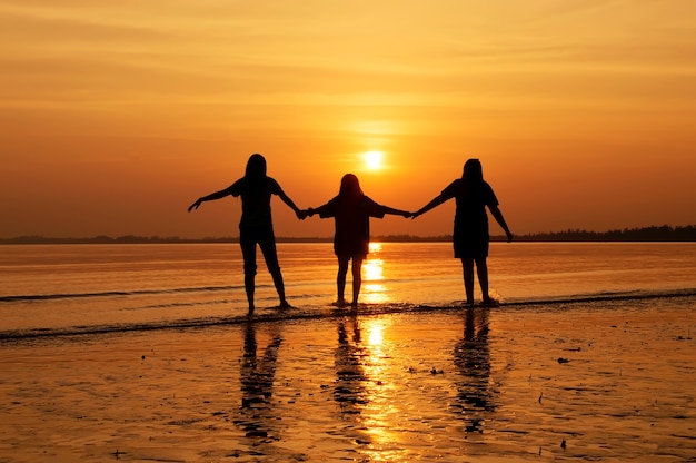 Siluetta della mano della holding del gruppo della ragazza che cammina sulla spiaggia al tramonto