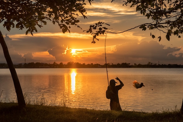 Siluetta della pesca del pescatore dal lato del fiume nel tramonto
