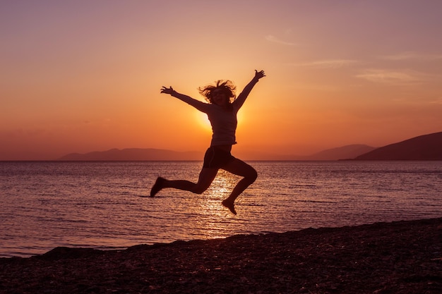 Siluetta della ragazza che salta con le mani sulla spiaggia al tramonto