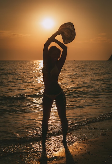 Siluetta della ragazza felice che gode al tramonto sulla spiaggia.