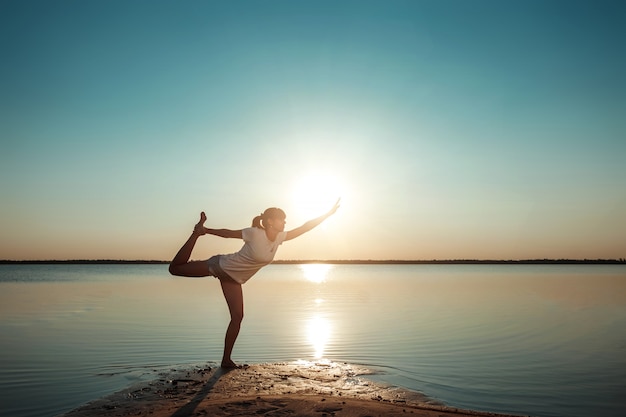 Siluetta della ragazza su un lago e su un bello tramonto