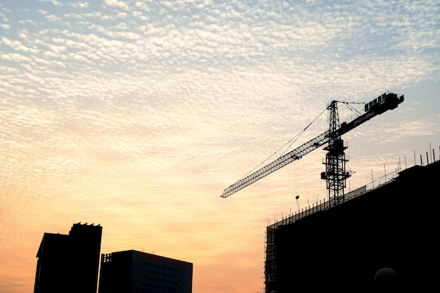 Siluetta della scena di tramonto con la gru a torre sulla costruzione del sito di costruzione