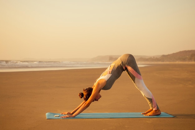 Siluetta di giovane donna in un vestito alla moda per la tuta di yogi che fa yoga sulla spiaggia nello spazio della copia di posa.