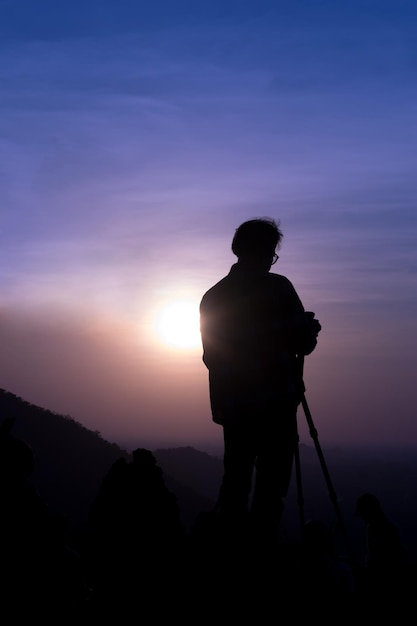 Siluetta di un fotografo che scatta foto del tramonto sulla cima della montagna