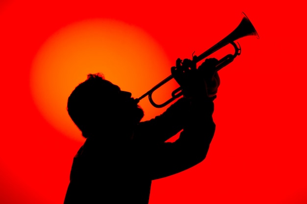 Siluetta di un musicista jazz che suona la tromba, isolata nel fondo rosso. Concetto di musica jazz.