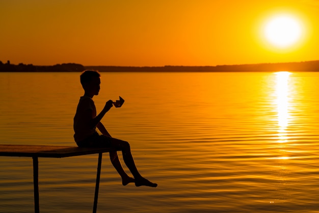 Siluetta di un ragazzo al tramonto vicino al fiume.