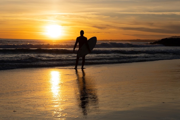 Siluetta di un surfista solitario che tiene la tavola da surf in riva al mare