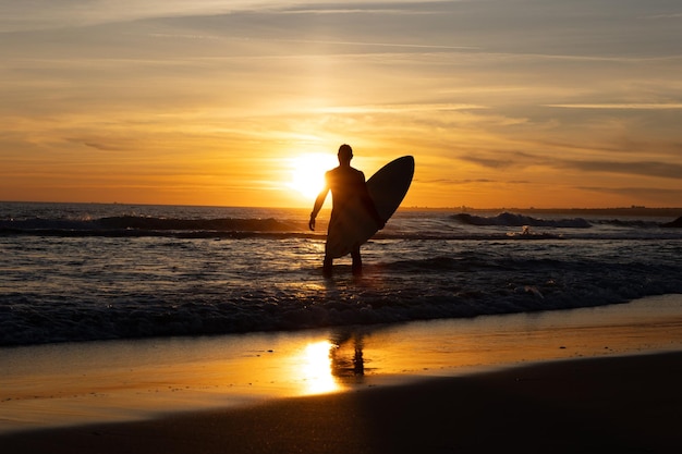 Siluetta di un uomo che tiene la tavola da surf in piedi in riva al mare al tramonto