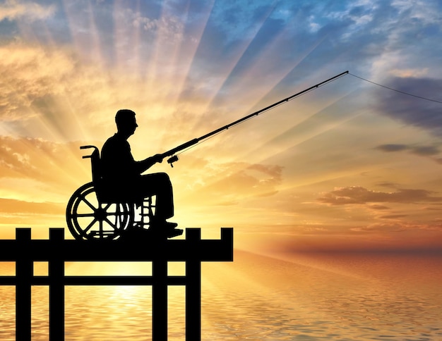 Siluetta di un uomo disabile in sedia a rotelle con una canna da pesca in mano che pesca vicino all'acqua. Concetto di svago e tempo libero delle persone con disabilità