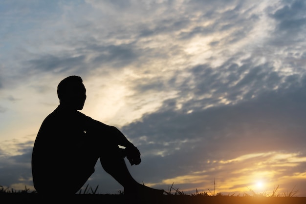 Siluetta di un uomo seduto con così triste al tramonto.