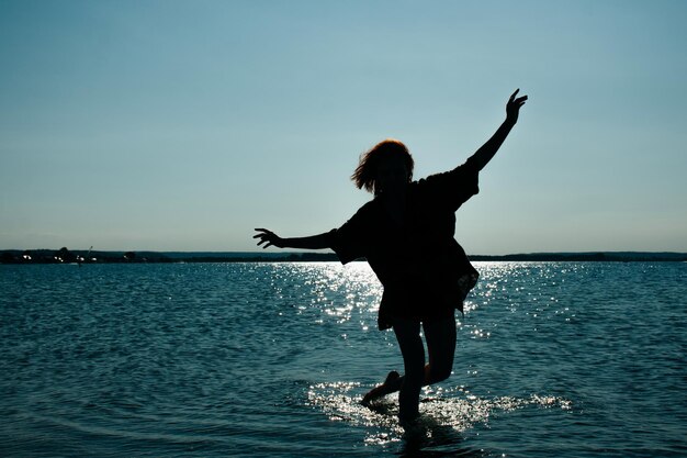 Siluetta di una donna al tramonto sul mare blu e sull'acqua splendente