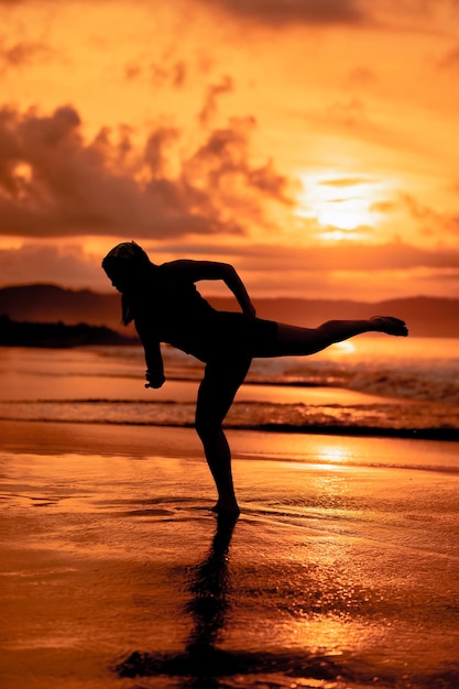 Siluetta di una donna asiatica che balla balletto con grande flessibilità e una vista delle onde dietro di lei