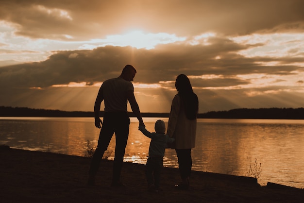 Siluetta di una famiglia con il figlio sulla spiaggia in estate in riva al fiume