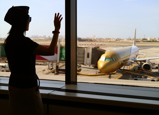 Siluetta di una mano d'ondeggiamento della donna all'aeroplano all'aeroporto