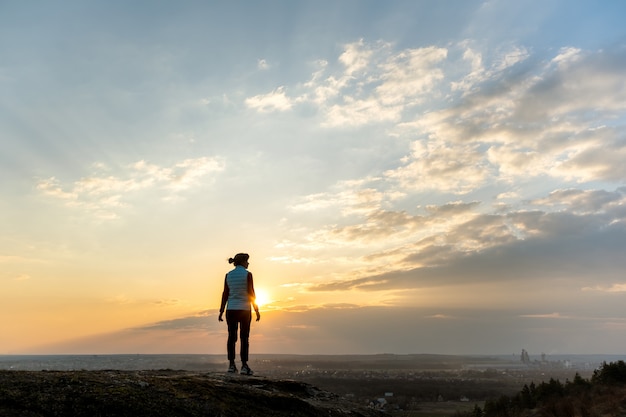 Siluetta di una viandante della donna che sta da solo godendo del tramonto all'aperto. Turista femminile sul campo rurale nella natura di sera. Concetto di turismo, viaggi e stile di vita sano.