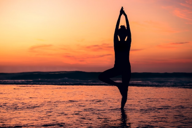 Siluetta di yoga di meditazione della donna sulla spiaggia del mare al tramonto