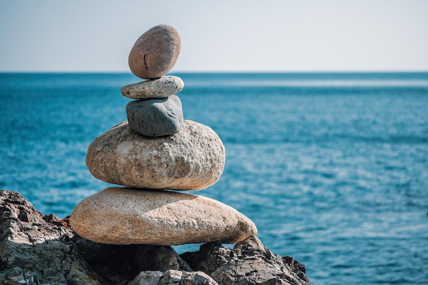 Siluetta equilibrata della piramide di ciottoli sul bokeh caldo astratto del tramonto della spiaggia con il mare sul