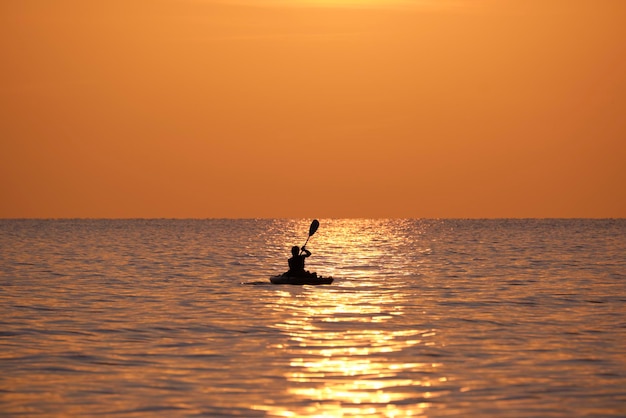 Siluetta scura del pescatore solitario che rema sulla sua barca sull'acqua di mare al tramonto