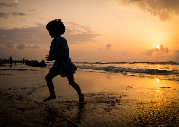 Siluette dei bambini che hanno tempo felice sulla spiaggia del mare vicino al tramonto