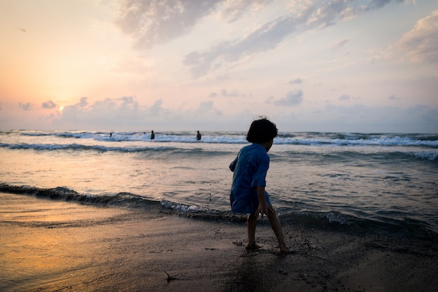 Siluette dei bambini che hanno tempo felice sulla spiaggia del mare vicino al tramonto