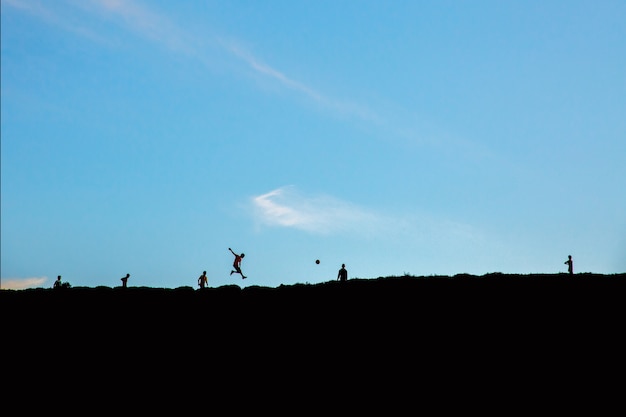 Siluette dei ragazzi che giocano con una palla sulla collina sotto il cielo blu