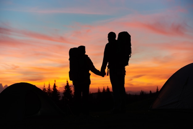 Siluette di una coppia amorosa che si tengono per mano stando sopra la montagna mentre facendo un'escursione