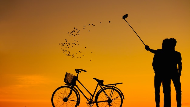 Siluette uomo e donna che prendono selfie con lo smartphone sul cielo al tramonto: foto della siluetta.