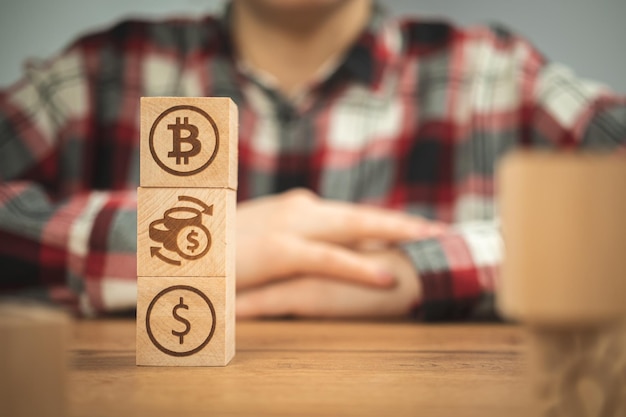 Simboli del dollaro di cambio bitcoin su un cubo di legno nelle mani Concetto di criptovaluta e sfondo contanti tavolo in legno