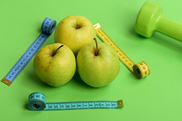 Simboli di sport e stile di vita sano. Modello fatto di frutti di mela vicino a bilancieri di colore verde / metro a nastro di colore blu ciano. Atletica leggera e concetto di perdita di peso. / Concetto di dieta e regime sportivo. /