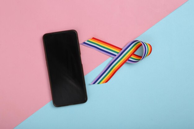 Simbolo del nastro dell'orgoglio del nastro arcobaleno LGBT con smartphone su sfondo blu rosa