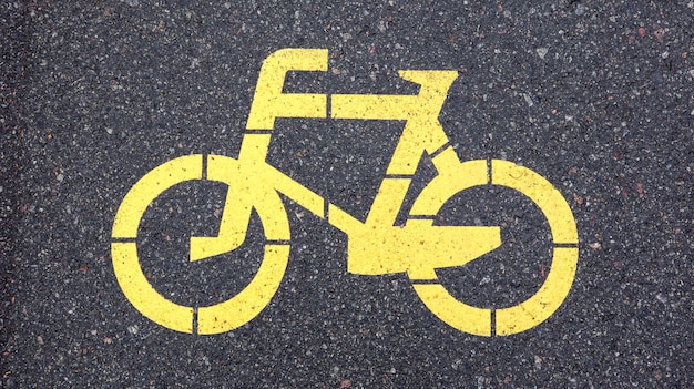 Simbolo della bicicletta che rappresenta un percorso per le biciclette. Cartello dipinto di giallo per biciclette sull'asfalto. Disposizione piana, vista dall'alto.