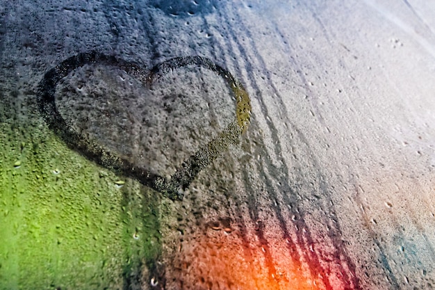 Simbolo di amore del cuore dipinto su vetro appannato illuminato da luci colorate