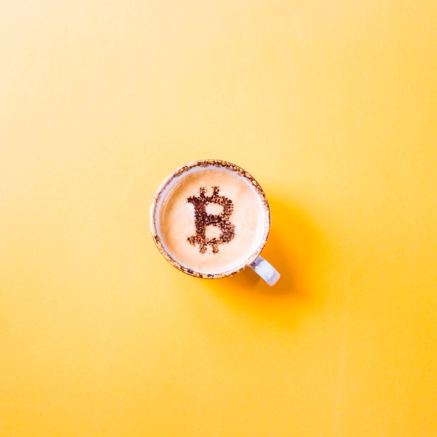 Simbolo di cripto valuta criptato su una tazza di caffè su uno sfondo giallo