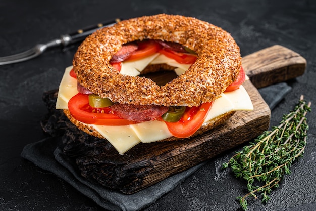 Simit bagel sandwich con lattuga, pomodoro, formaggio giallo e prosciutto. Sfondo nero. Vista dall'alto.