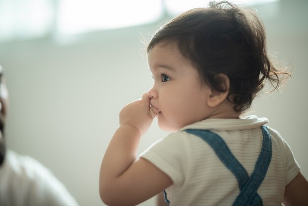 Simpatica bambina giocosa che impara a camminare e stare in piedi sostenendosi al divano di casa mentre distoglie lo sguardo maliziosamente