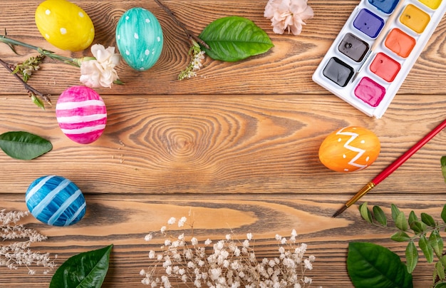 Simpatiche uova di Pasqua colorate dipingono e spazzolano fiori e foglie di primavera su uno sfondo di legno Spazio di copia