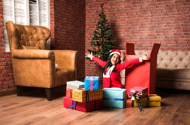 Simpatici bambini asiatici indiani che festeggiano il Natale a casa con cappello da Babbo Natale, regali e albero di Natale