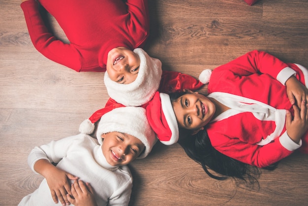 Simpatici bambini asiatici indiani che festeggiano il Natale a casa con cappello da Babbo Natale, regali e albero di Natale