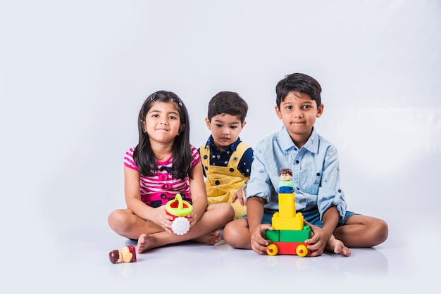 Simpatici bambini indiani o asiatici che giocano con giocattoli o blocchi e si divertono seduti a tavola o isolati su sfondo bianco