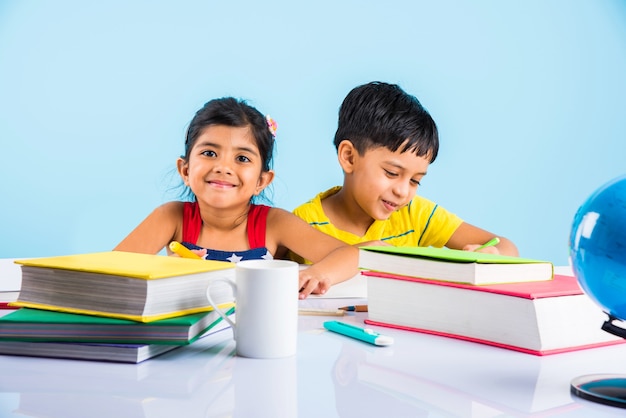 Simpatici bambini indiani o asiatici che studiano sul tavolo da studio con una pila di libri, globo educativo, isolato su colore azzurro