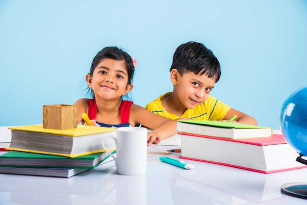 Simpatici bambini indiani o asiatici che studiano sul tavolo da studio con una pila di libri, globo educativo, isolato su colore azzurro